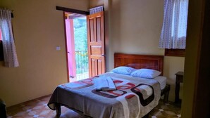 Un dormitorio con cama, cabecero de madera, ventana con cortinas y puerta que da al exterior.