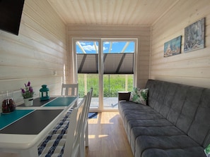 A cozy room with a sofa, a small table, a chair, a potted plant, and a painting on the wall. - Comfortable Holiday Homes With air Conditioning (Darlowo)