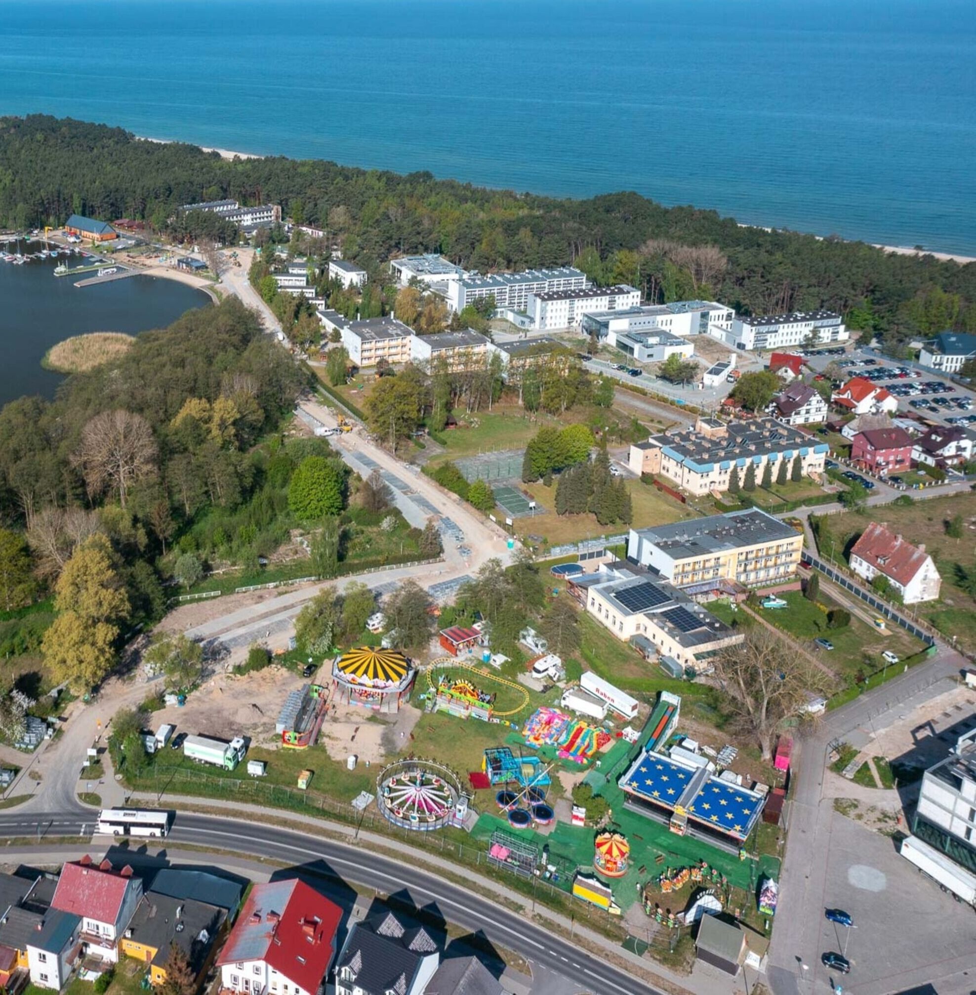 Luftaufnahme einer Küstenlandschaft mit Strand, See und einem Park mit Fahrgeschäften.