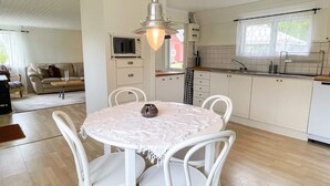 Een compacte keuken met witte kasten, een ronde eettafel met witte stoelen, een hanglamp en een magnetron op het aanrecht.