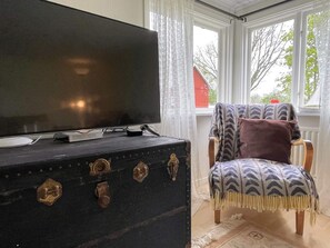 A room with a television on a dresser, a chair with a patterned throw, and a window with a view of trees. - 6 Person Holiday Home in Lottorp (Löttorp)