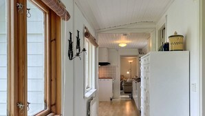 Een smalle gang met een raam met houten kader, een witte radiator en een witte koelkast.