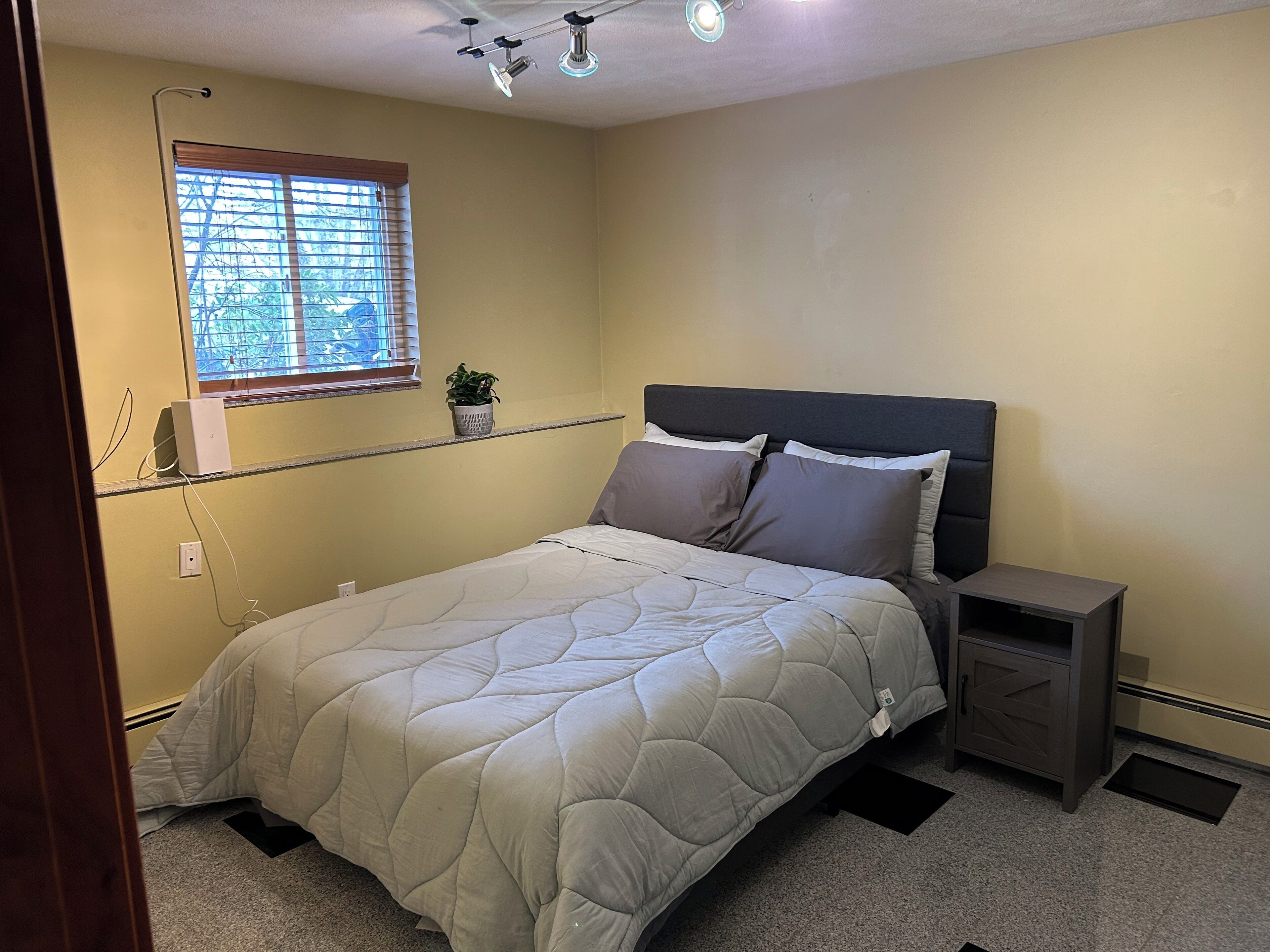 Une chambre à coucher comprenant un lit, une table de chevet, une commode, une fenêtre et un ventilateur de plafond.
