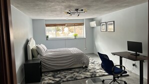 A bedroom with a bed, a desk, a chair, a window, and an air conditioner. - Private Luxury 2 Bedroom Suite (Framingham)