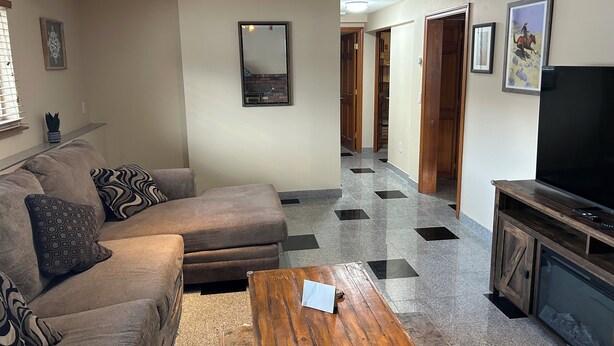 A living room with a sofa, a coffee table, a TV, and a hallway leading to other rooms. - Private Luxury 2 Bedroom Suite (Framingham)