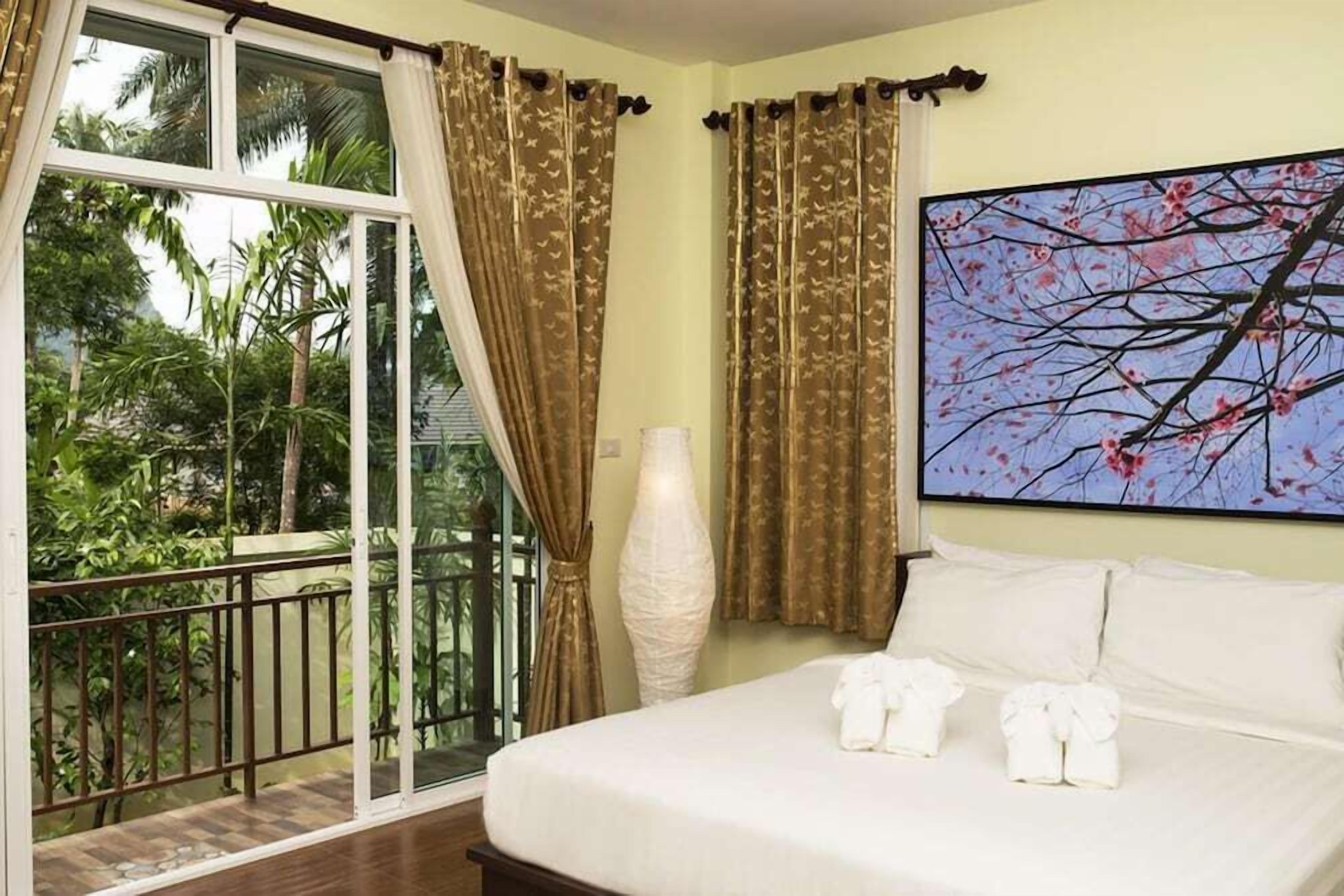 A bedroom with a bed, a large window with curtains, a painting, and a vase.