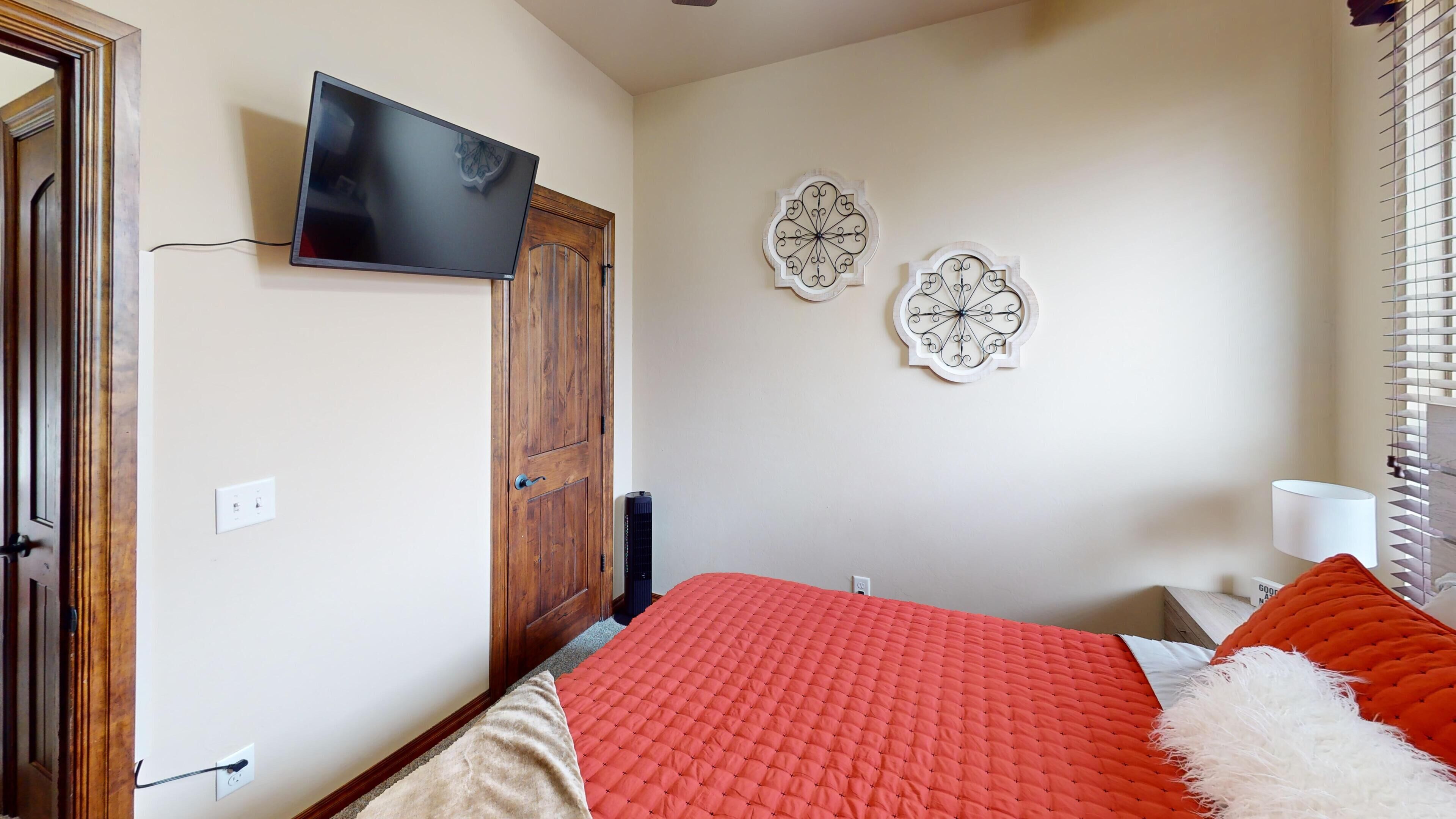 A bedroom with a bed, a TV mounted on the wall, and two decorative wall pieces.