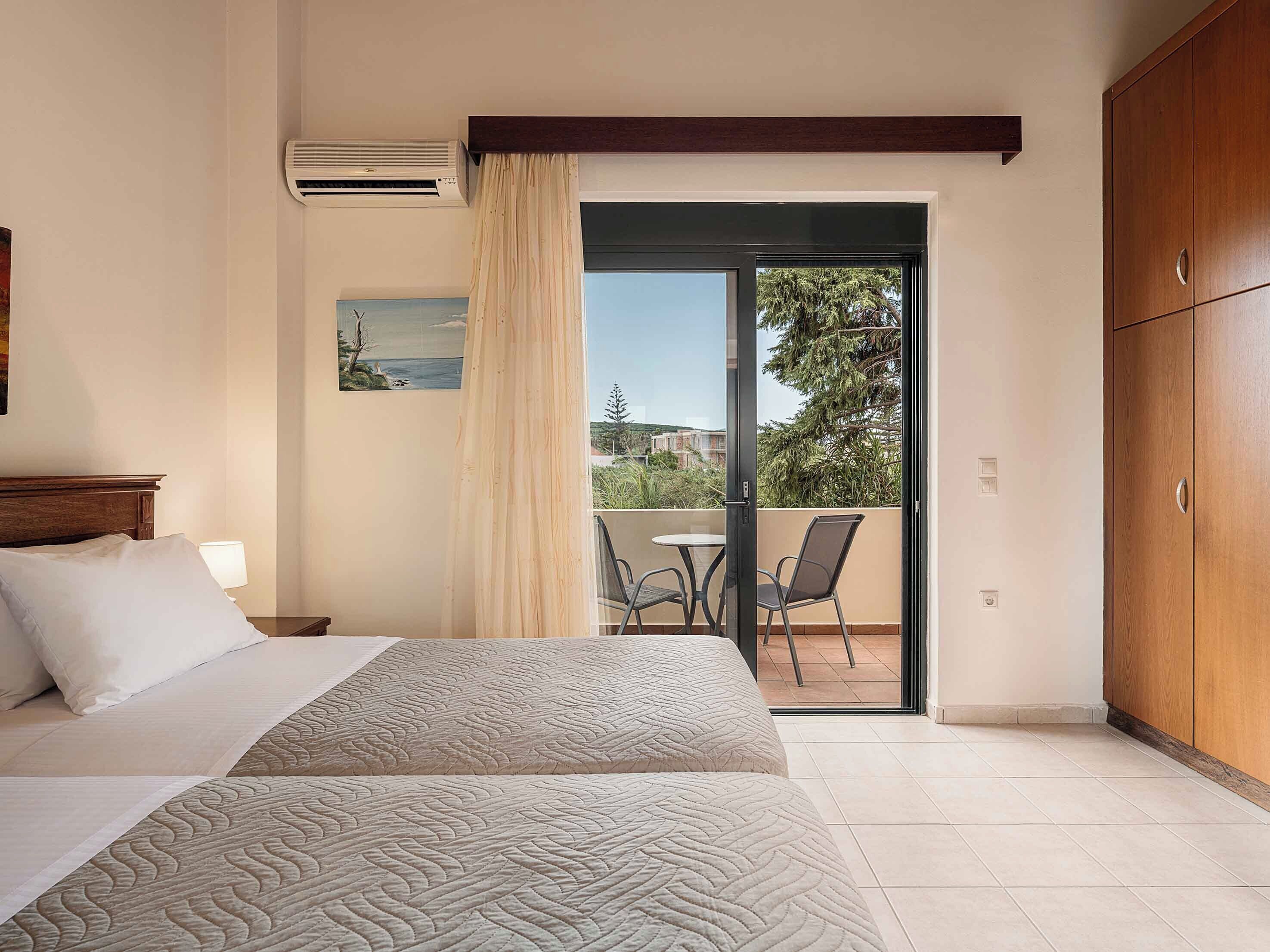 A bedroom with a bed, a painting, an air conditioner, a balcony with chairs, and a wooden wardrobe.