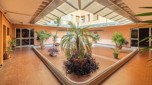 A spacious atrium with a high ceiling, potted plants, and a tiled floor. - Posta Suites - 1br/4p - a Ventimiglia (Ventimiglia)