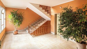 A spacious room with a herringbone-patterned floor, a wooden staircase with a metal railing, and two potted plants. - Posta Suites - 1br/4p - a Ventimiglia (Ventimiglia)
