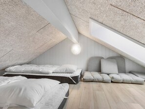 Quarto com teto inclinado, cama, sofá e luminária fixada na parede.