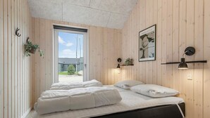 A bedroom with a bed, a window, a wall-mounted shelf with a plant, and a framed picture. - 5 Star Holiday Home in Glesborg (Glesborg)