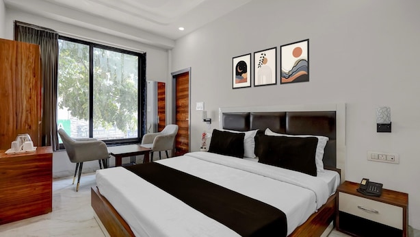 A modern hotel room with a large bed, a desk, a chair, and a window with curtains.