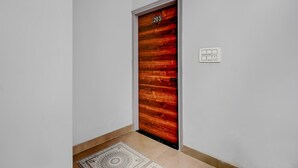 A hallway with a wooden door marked '203,' a patterned rug, and a light switch on the wall.