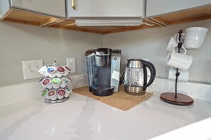 Ett kök med en kaffebryggare, en vattenkokare och ett hyllsystem för kaffemuggar.