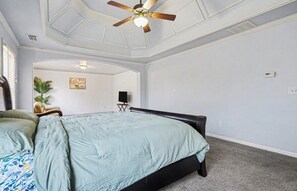 Un dormitorio con una cama, un ventilador de techo, una planta y un cuadro en la pared.
