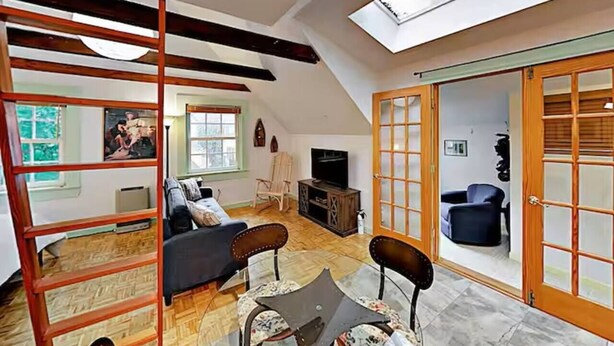 A loft-style living room with a high ceiling, a skylight, a sofa, a coffee table, and a TV. - Entire 4-Unit House - Downtown Bar Harbor (Bar Harbor)