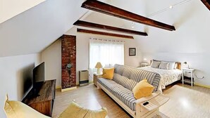 A modern loft bedroom with a sloped ceiling, a sofa bed, a TV, and a brick accent wall. - Entire 4-Unit House - Downtown Bar Harbor (Bar Harbor)