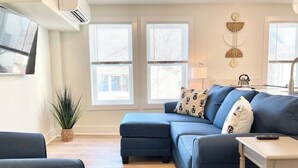Ein modernes Wohnzimmer mit Ecksofa, einem kleinen Tisch und einem Blumentopf.