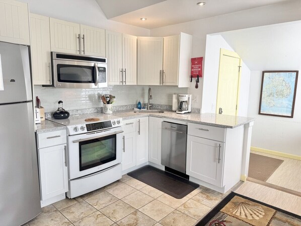 A modern kitchen with white cabinets, stainless steel appliances, and a tiled backsplash. - Sunset Studio in the Heart of Bar Harbor (Bar Harbor)