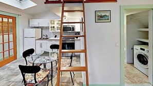 Eine kompakte Wohnung mit Schlafgalerie, einem Essbereich mit Glastisch sowie einer Küche mit weißen Schränken und integriertem Mikrowellenherd.