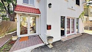 Ein zweistöckiges Haus mit rotem Dach, einer Haustür mit Glasschilden und einer kleinen Veranda mit zwei Pflanzgefäßen.
