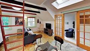 Ein Loft-Wohnzimmer mit hoher Decke, Holzbalken, einem Oberlicht, einer Couch, einem Fernseher und einer Schiebeglasdoor.