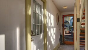 A hallway with a white door, a window, and a view of a residential area outside. - Radiant Studio in the Heart of Bar Harbor (Bar Harbor)