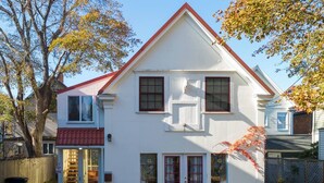 A two-story white house with a red roof, a garage with a red awning, and a small porch with a flower box. - Cozy Studio in the Heart of Bar Harbor (Bar Harbor)