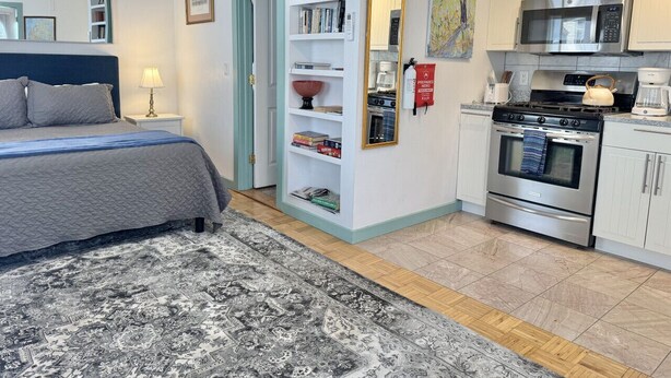 A bedroom with a bed, bedside table, lamp, and a large rug. - Cozy Studio in the Heart of Bar Harbor (Bar Harbor)