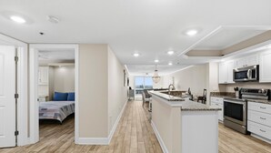Une cuisine moderne avec des meubles blancs, un îlot central, des appareils en acier inoxydable et un plancher en bois.