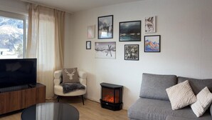 Una sala de estar con televisor, sofá, sillón, chimenea y obras de arte en la pared.