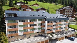 Un hotel de varios pisos con diseño moderno, con balcones, un estacionamiento y vistas al paisaje verde circundante.
