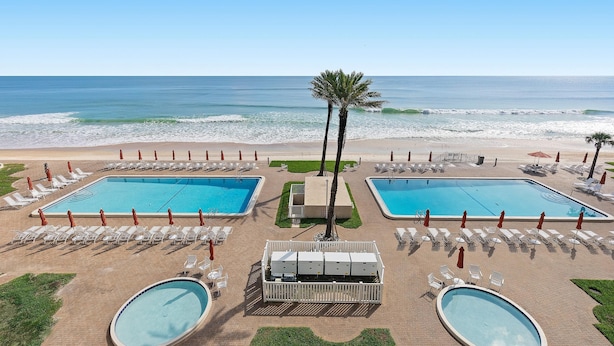 A resort pool area with two rectangular pools, a palm tree, and beach views. - Sandpiper 611 (New Smyrna Beach)
