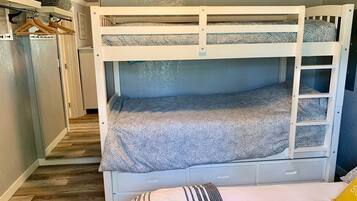 Een stapelbed met een bedspread met patroon, een klein lade en een kledingrek met kleding.