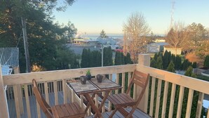 Una terraza de madera con una mesa y sillas, con vista a una zona residencial con casas y árboles.