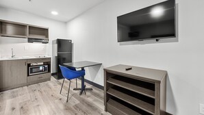 A modern kitchen with built-in appliances, a dining area with a blue chair, and a flat-screen TV mounted on the wall. - Southern Suites Atlanta-Wendell (Atlanta)
