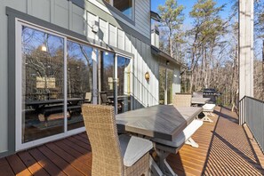 An outdoor deck with a wooden table and chairs, large sliding glass doors, and a view of trees. - Mountain View • Hot Tub • Sauna • Fire Pit (Blue Ridge)
