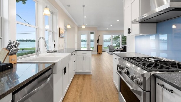 Een moderne keuken met witte kastjes, een roestvrijstalen fornuis en een groot raam met uitzicht op het water.