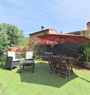 Une terrasse extérieure avec des chaises en osier, une table et un grand parasol.
