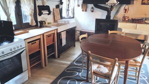 A kitchen with a stove, sink, wooden cabinets, a dining table with chairs, and a patterned rug.