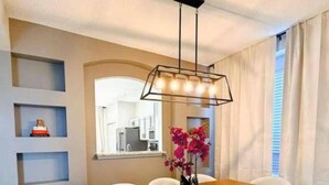 Een eetruimte met een houten tafel, zes stoelen, een hanglamp en een raam met gordijnen.
