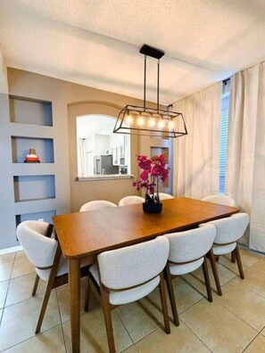 A dining area with a wooden table, six chairs, a hanging light fixture, and a window with curtains. - 7 Bd/ 4.5 Bath- Terra Verde Resort (Kissimmee)