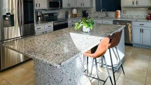 Een moderne keuken met granieten aanrechtbladen, roestvrijstalen apparatuur en een centraal kookeiland met barkrukken.