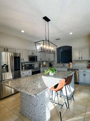 A modern kitchen with granite countertops, stainless steel appliances, and a central island with bar stools. - 7 Bd/ 4.5 Bath- Terra Verde Resort (Kissimmee)