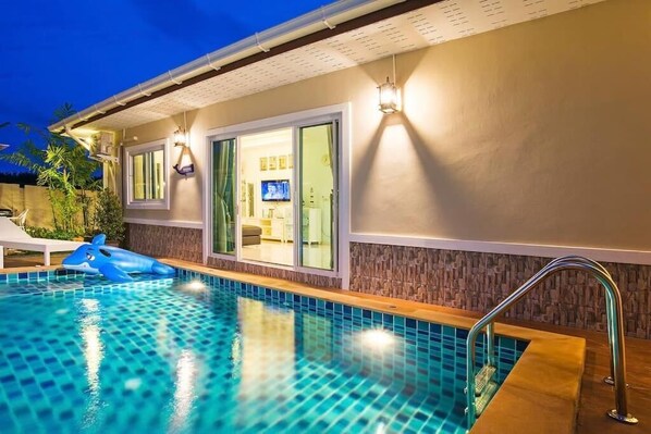 En pool med en blå hajsvømmer, en overdækket terrasse og et fjernsyn i baggrunden.