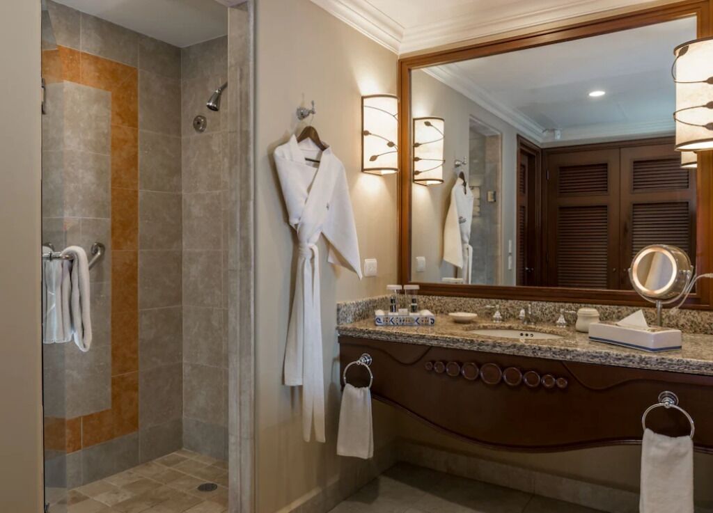 Un baño con cabina de ducha, tocador con espejo grande y dos anillas para toallas.