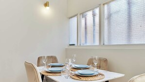 Ein Esstisch mit Tellern, Gläsern und Platzsets, nahe einem Fenster mit Jalousien.