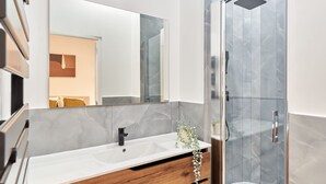 Ein modernes Badezimmer mit einem großen Spiegel, einem weißen Waschbecken, einem Holzkabinett und einer Duschkabine aus Glas.