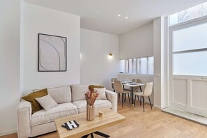 A modern living room with a sofa, coffee table, and dining area. - Charming AC Apartment - Buttes Chaumont Park (Paris)